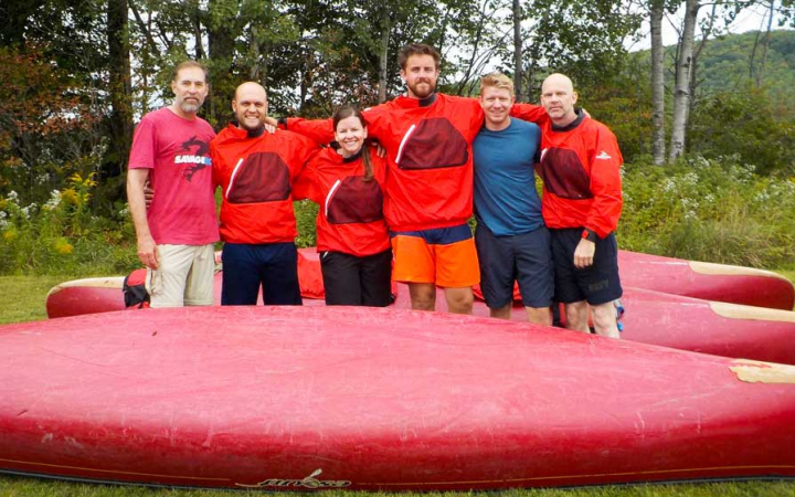 a group of veterans with their arms around each other smile at the camera while standing between canoes